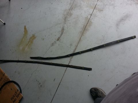 1994 Ford Bronco - Two detached black rubber trim pieces with yellow clips lie on a concrete floor.