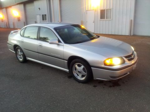 2001 Chevrolet Impala - A silver sedan is parked in front of a warehouse with its headlights on.