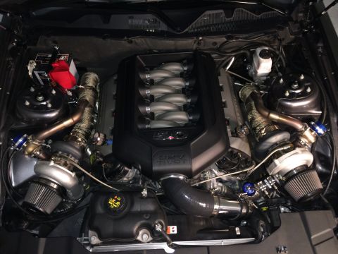 2013 Ford Mustang - Engine bay view of a twin-turbocharged V8 engine, identified by the "5.0 COYOTE" badge, consistent with a 2013 Ford Mustang.