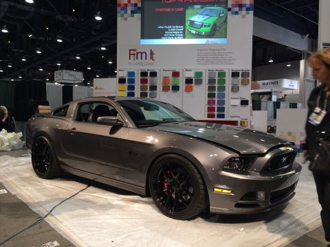 2013 Ford Mustang - A gray Ford Mustang is displayed at an automotive event with various vinyl wrap color samples in the background.