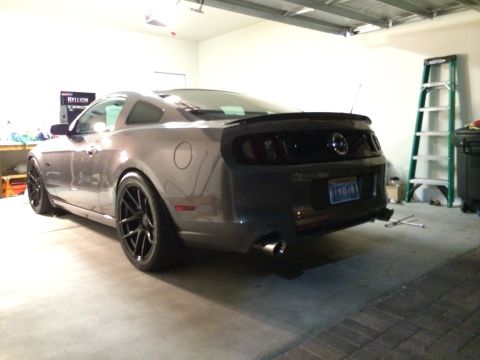 2013 Ford Mustang - The rear of a gray 2013 Ford Mustang is visible in a garage, aftermarket wheels and a spoiler.