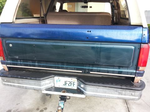 1994 Ford Bronco - The rear view of a 1994 Ford Bronco, a blue tailgate and a white removable roof section.