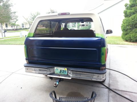 1994 Ford Bronco - The rear of a two-tone Ford Bronco shows a two-tone paint job with a green accent stripe and a chrome bumper.