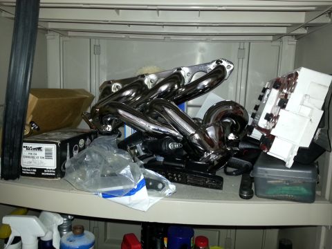 1994 Ford Bronco - Chrome exhaust headers are stored on a shelf with various boxes and containers.