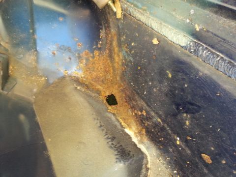 1994 Ford Bronco - Close-up of significant rust damage and a hole in a vehicle's metal panel.