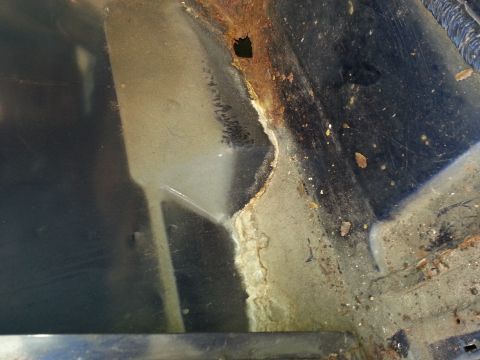 1994 Ford Bronco - Close-up of a rusted interior panel with dirt and debris, showing signs of wear and tear.