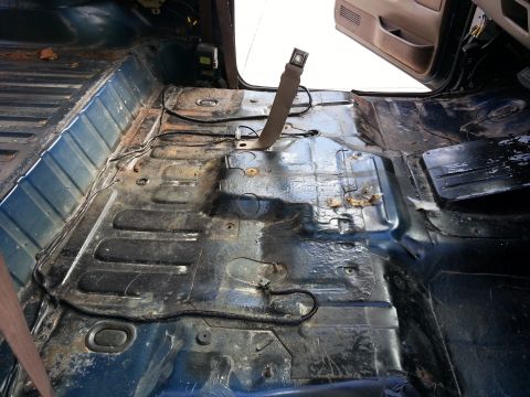1994 Ford Bronco - The bare interior floor of a vehicle, stripped of its seats and carpeting, reveals rust and wiring.