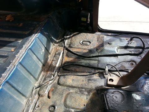 1994 Ford Bronco - bare metal floor pan of a vehicle cab showing surface rust and exposed wiring with the interior stripped out.
