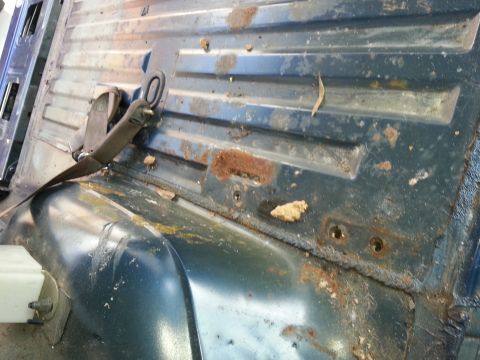 1994 Ford Bronco - Interior floor pan shows significant rust and wear, with a seatbelt assembly attached.