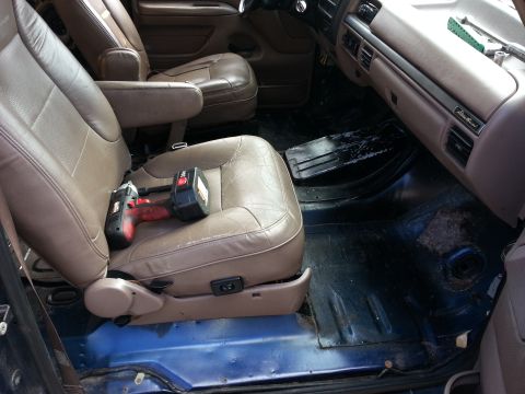 1994 Ford Bronco - The interior of a vehicle shows tan leather seats and a drill placed on the driver's seat.