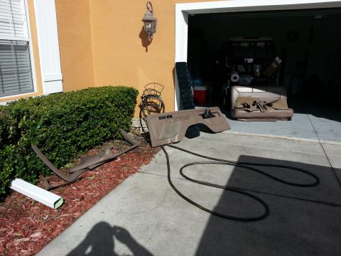 1994 Ford Bronco - Removed tan interior door panel, seat and trim pieces drying on a driveway beside a garage, with a coiled air hose.