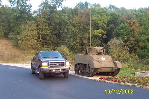 2000 Ford F-250 - A Ford pickup truck is parked on a paved surface next to a military tank with a white star emblem.
