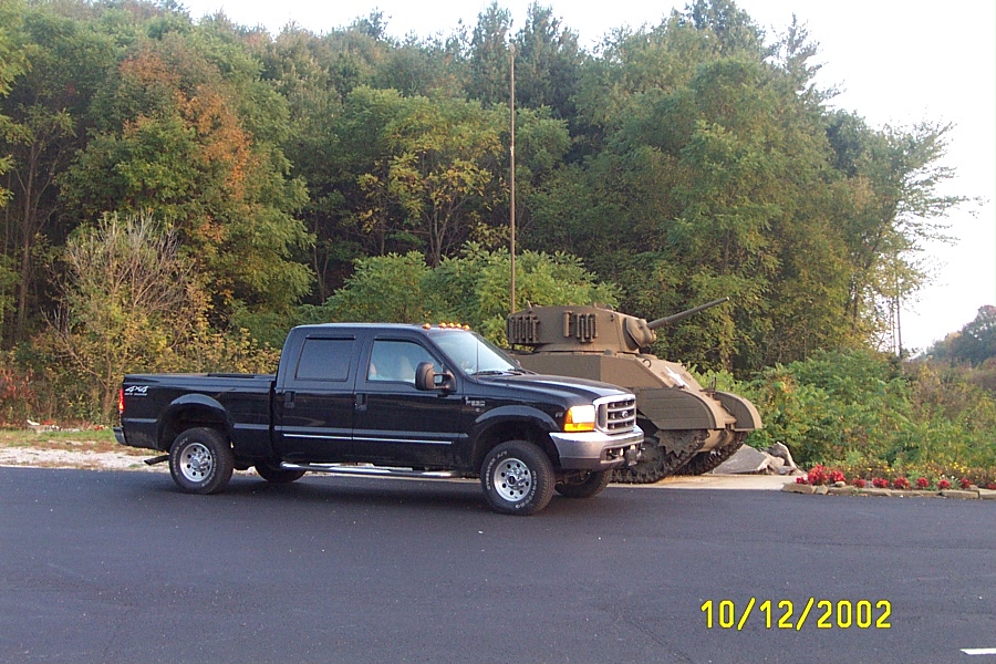 Black Ford Super Duty crew cab 4x4 pickup parked in profile next to a display tank