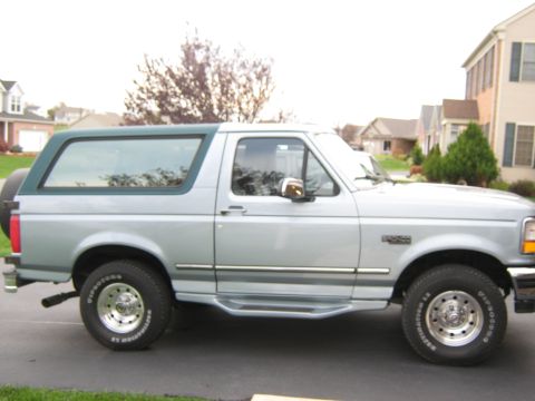 1996 Ford Bronco - This 1996 Ford Bronco is shown from the side, parked in a suburban driveway with houses in the background.