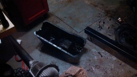 1979 Ford Bronco - A detached oil pan sits on a garage floor, covered in dark residue.