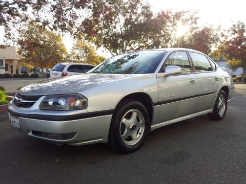 2001 Chevrolet Impala - A silver 2001 Chevrolet Impala is parked on asphalt with a white van and trees visible.