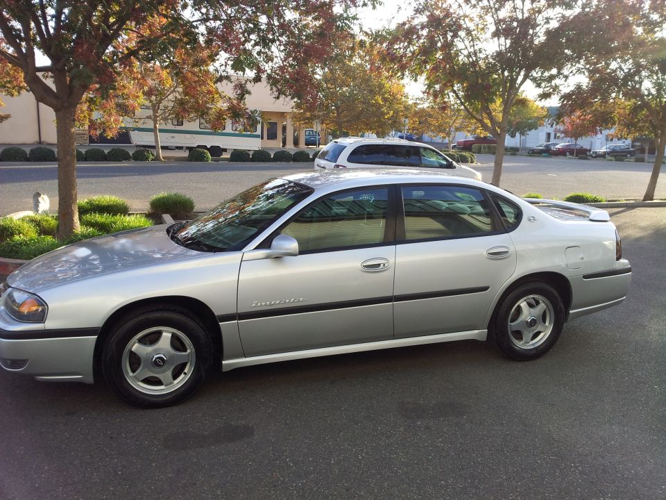 Silver sedan parked on asphalt, side view. Visible text: SUPERMOTORS.NET
