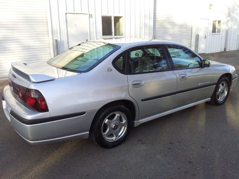 2001 Chevrolet Impala - A silver sedan is parked outside a commercial building. The car has tinted windows and a spoiler.