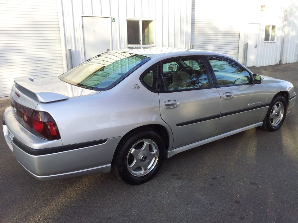 Silver sedan parked outside a building. It has a spoiler on the trunk