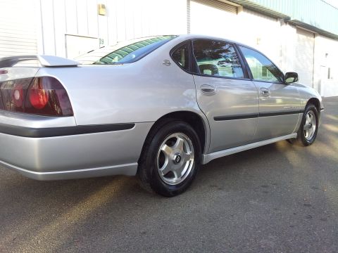 2001 Chevrolet Impala - Silver sedan with a spoiler and tinted taillights is parked outside a building.