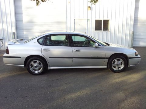 2001 Chevrolet Impala - Side profile of a silver 2001 Chevrolet Impala sedan parked in front of a white building.