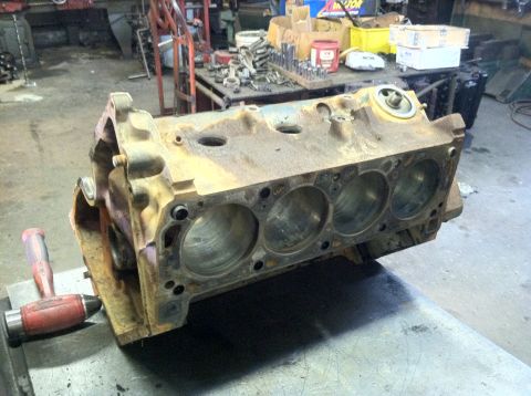 1978 Ford Bronco - An engine block sits on a workbench in a cluttered garage setting.