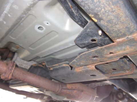 2001 Ford Crown Victoria - The undercarriage of a vehicle, revealing its structural components and exhaust system with signs of wear and tear.