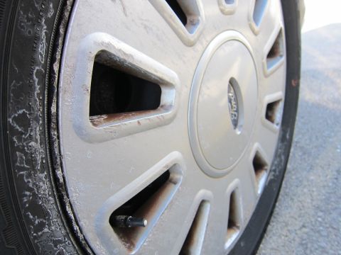 2001 Ford Crown Victoria - Close-up of a worn silver wheel and tire, displaying a Ford emblem and salt buildup.