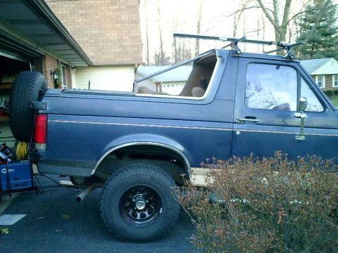 1990 Ford Bronco - Side view of a blue 1990 Ford Bronco, equipped with a spare tire and a roof rack.