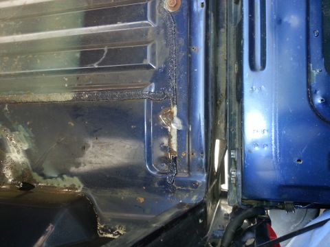 1994 Ford Bronco - Detail of rust and repair work on a vehicle's blue body panels.