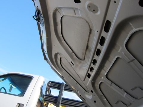 2001 Ford Crown Victoria - The underside of a car hood is shown against a bright blue sky, with a portion of a white truck visible to the left.