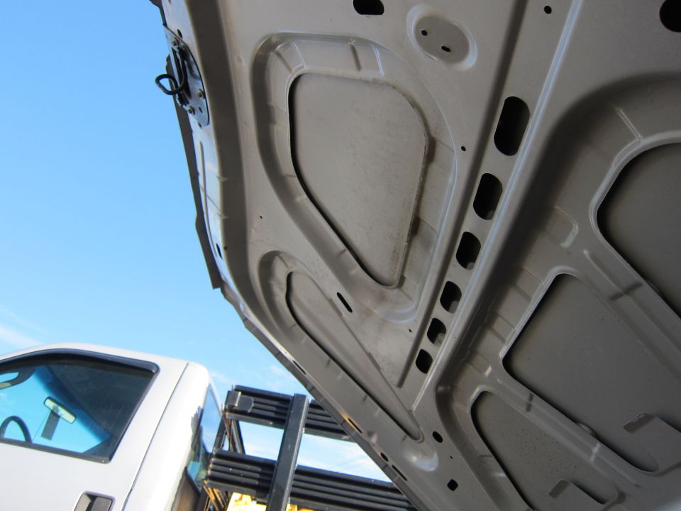 Underside of white car hood, blue sky, part of white truck visible