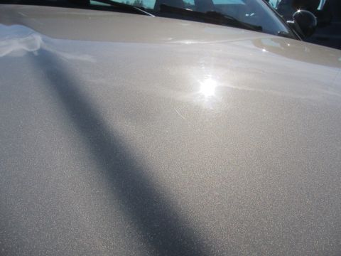 2001 Ford Crown Victoria - Close-up of a silver car's hood, showing the metallic paint finish under bright sunlight.