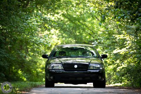 2003 Mercury Marauder - A black 2003 Mercury Marauder is captured from the front, driving down a road flanked by lush green trees.