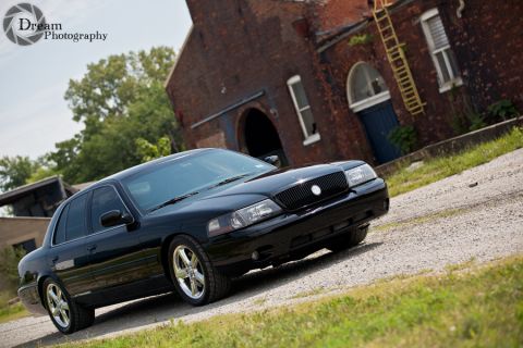 2003 Mercury Marauder - A black 2003 Mercury Marauder is captured in a three-quarter front view, parked on a gravel surface before an old brick structure.