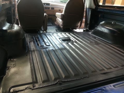1994 Ford Bronco - View behind the front seats of a truck cab showing a bare ribbed metal floor with carpet and trim removed.