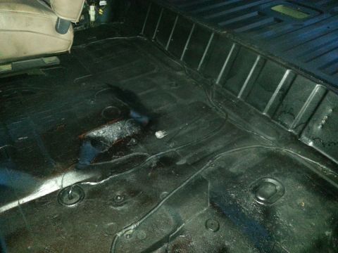 1994 Ford Bronco - The interior floor of a vehicle, showing black carpeting and a portion of a tan seat, is visible in this image.