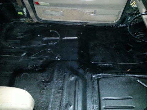 1994 Ford Bronco - The interior floor of a vehicle, coated in black, with wiring visible.