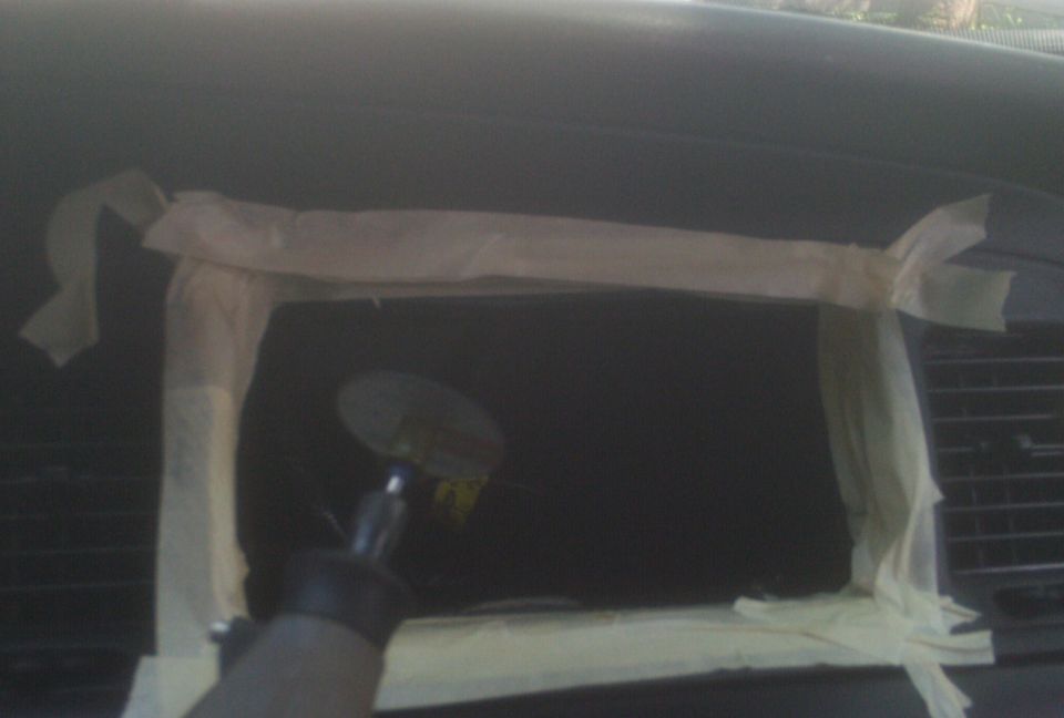 Dashboard interior with masking tape around a dark rectangular area, a circular sticker is visible on the tape, and a Supermotors logo is in the lower right