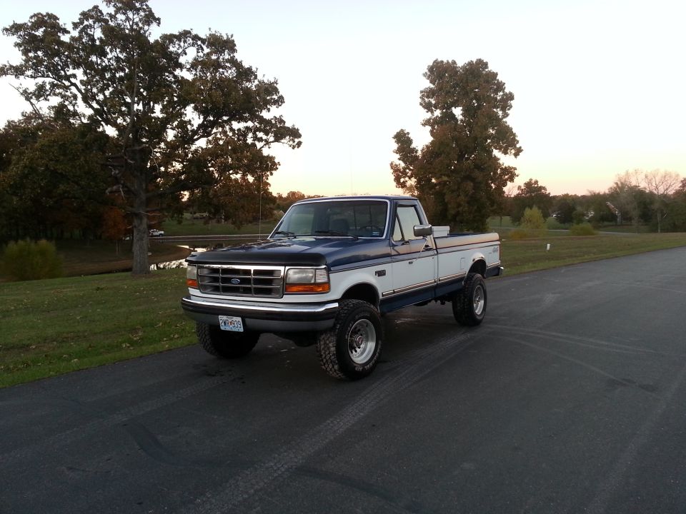 Two-tone blue and white Ford F-250 pickup truck with lifted suspension and chrome wheels parked on asphalt