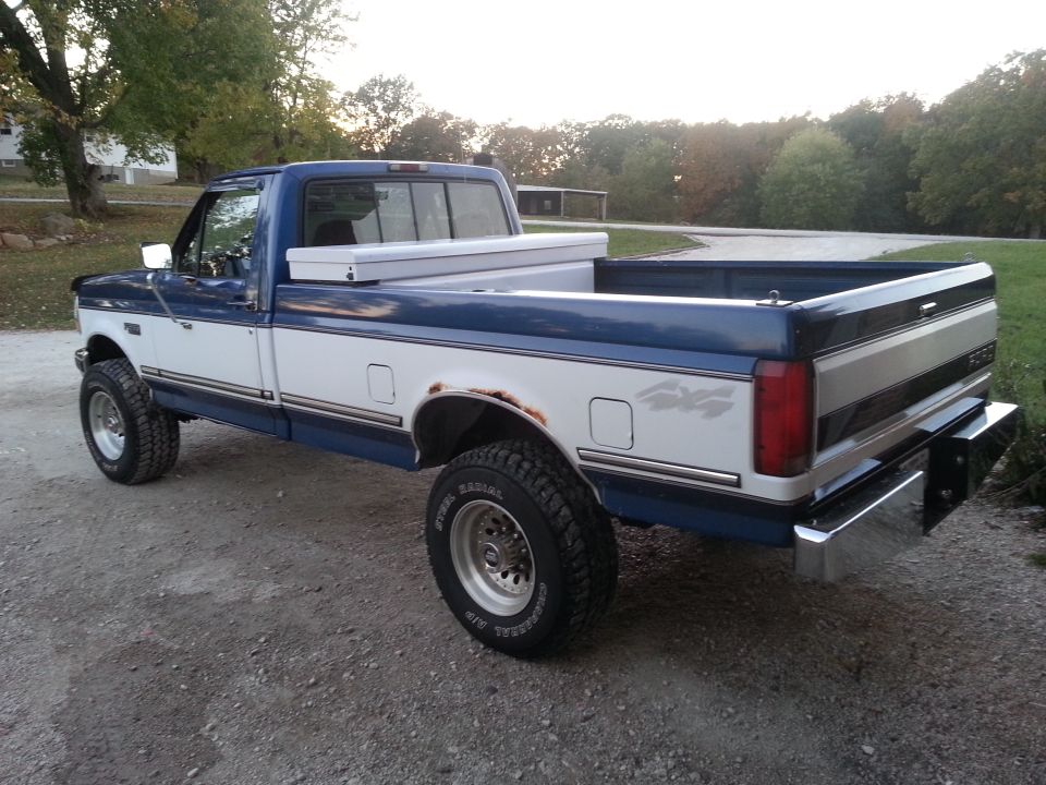 Two-tone blue and white Ford F-250 pickup truck with a toolbox in the bed, seen from the rear quarter