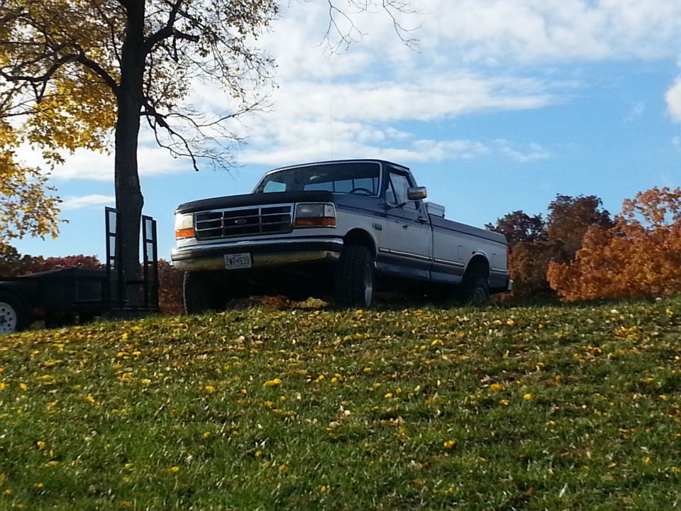 Two-tone pickup truck parked on a grassy hill with fall foliage