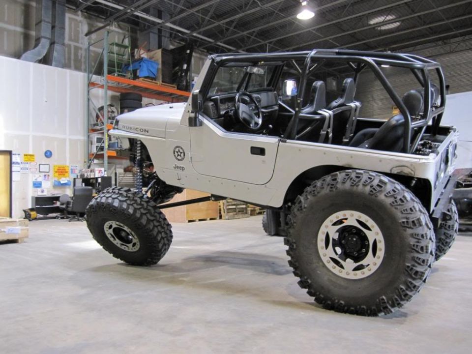 White Jeep Wrangler with roll cage and large off-road tires. Rubicon badge visible