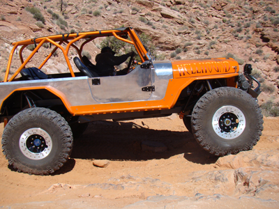 1985 Jeep CJ7 - This heavily modified Jeep CJ navigates a rocky trail with its custom roll cage and large off-road tires.