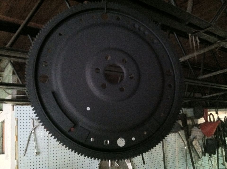 Black flywheel with gear teeth, hanging from ceiling in garage