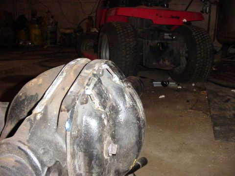 1992 Ford Bronco - A close-up view of a differential housing with visible welding repairs, with a red riding mower in the background.