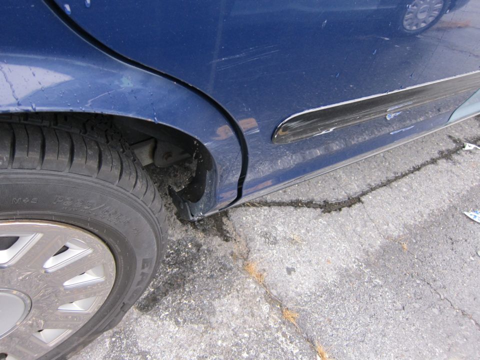 Blue sedan's rear door and wheel, showing scratches and damage to the trim