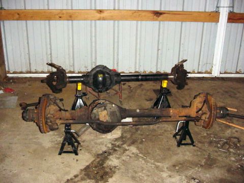 1992 Ford Bronco - Two vehicle axles are displayed on jack stands, one appearing newer and black, the other showing significant rust.