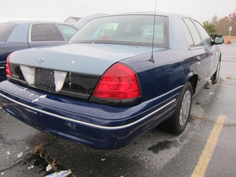 2001 Ford Crown Victoria - The rear of a blue Ford Crown Victoria is shown parked next to another vehicle on a wet day.