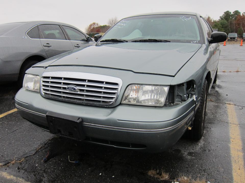 Front view of a 2001 Ford Crown Victoria with a damaged headlight assembly. Another car is parked to its left